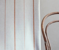 Berit-NAT Terracotta - curtain fabric with Orange striped print next to a chair to illustrate how your striped curtains would look.