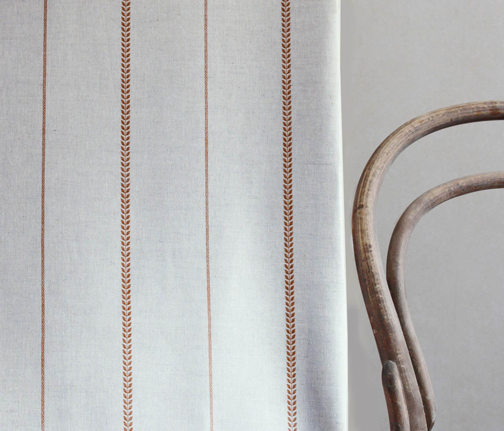 Berit-NAT Terracotta - curtain fabric with Orange striped print next to a chair to illustrate how your striped curtains would look.