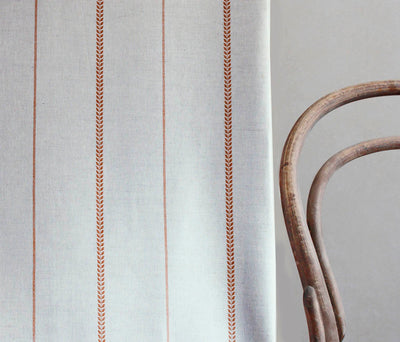 Berit-NAT Terracotta - curtain fabric with Orange striped print next to a chair to illustrate how your striped curtains would look.